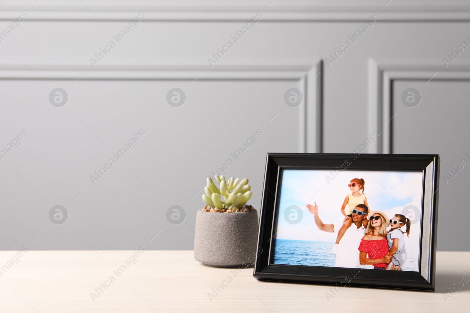 Photo of Frame with family photo and houseplant on white table near grey wall, space for text
