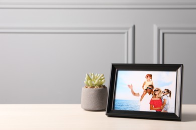 Frame with family photo and houseplant on white table near grey wall, space for text