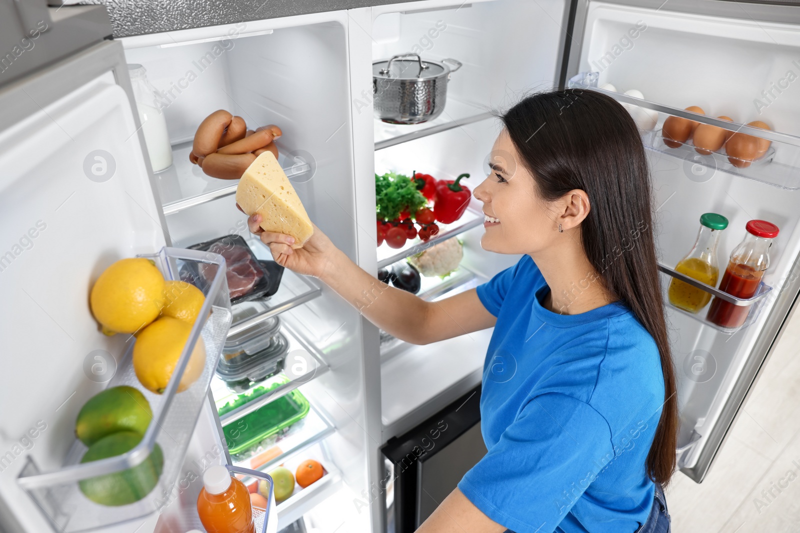Photo of Young woman taking cheese out of refrigerator indoors, above view
