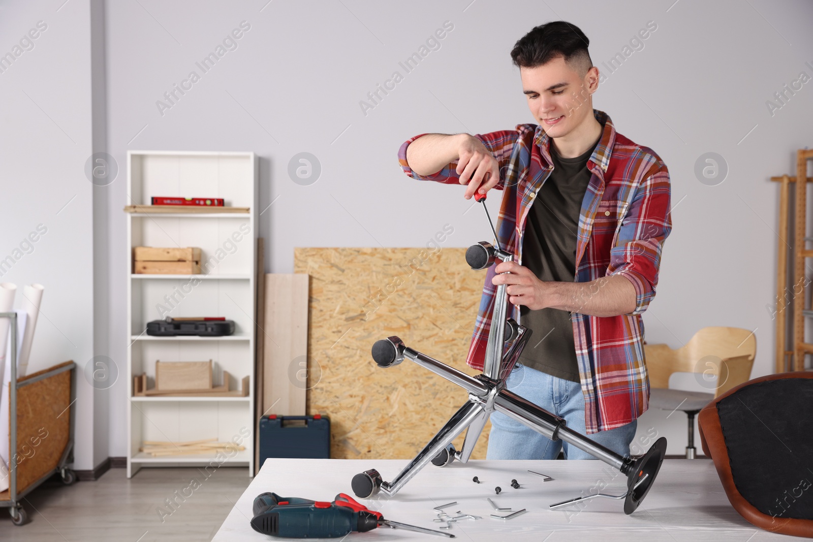 Photo of Young handyman repairing desk chair in room