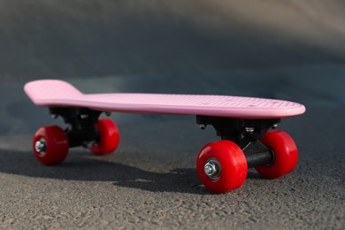 Photo of Modern pink skateboard with red wheels on asphalt road outdoors