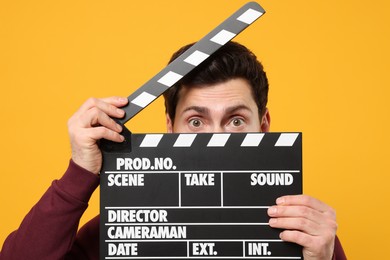 Surprised actor holding clapperboard on orange background
