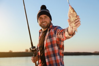 Photo of Fisherman with rod and caught fish at riverside