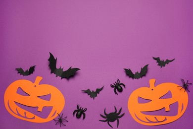 Flat lay composition with spooky paper pumpkins, spiders and bats on purple background, space for text. Halloween celebration