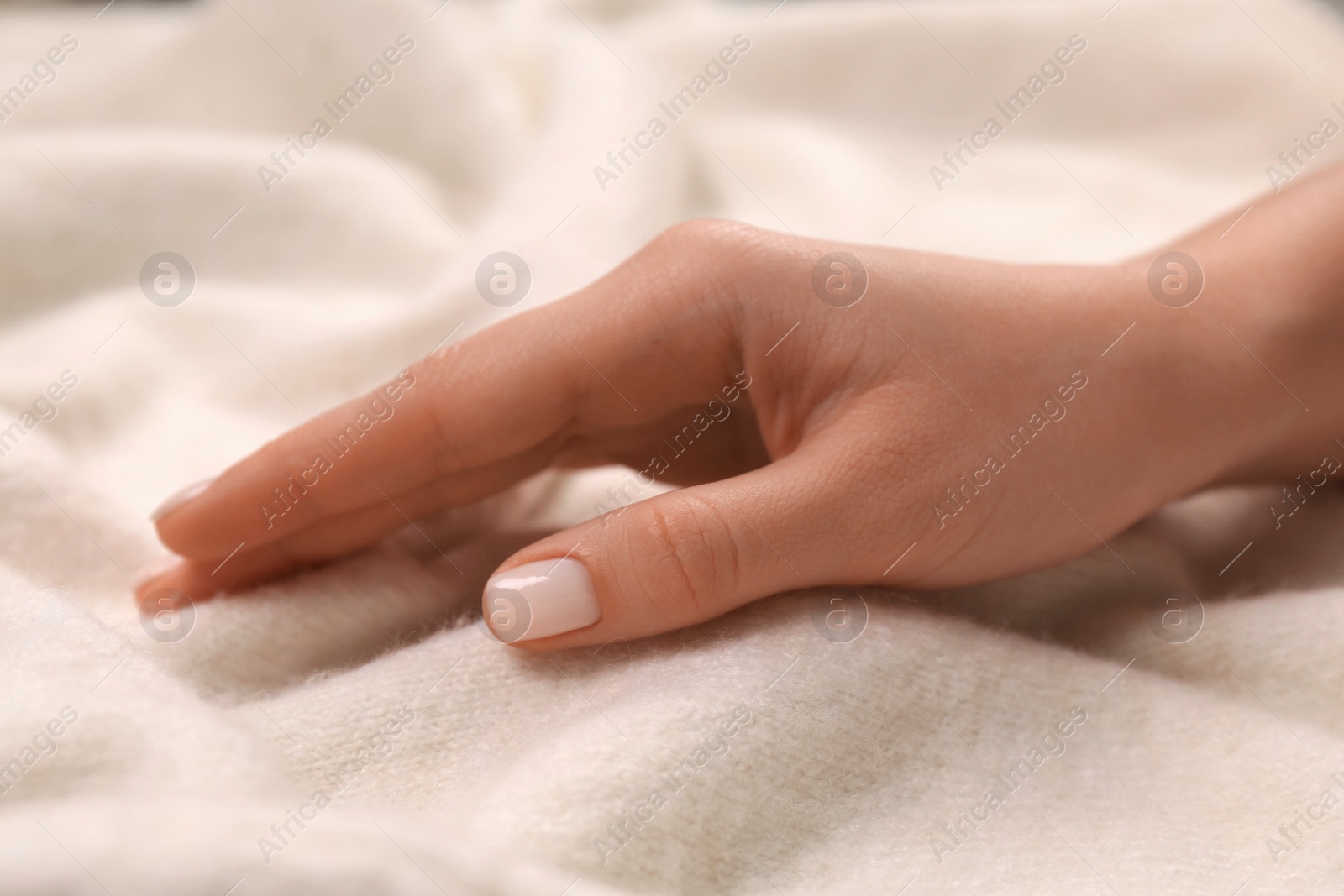 Photo of Woman touching soft beige knitted fabric, closeup