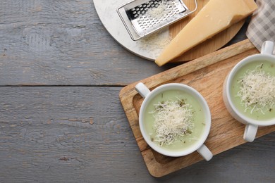 Delicious cream soup with parmesan cheese in bowls on grey wooden table, flat lay. Space for text