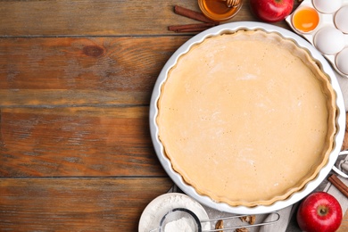 Raw dough and traditional English apple pie ingredients on wooden table, flat lay. Space for text