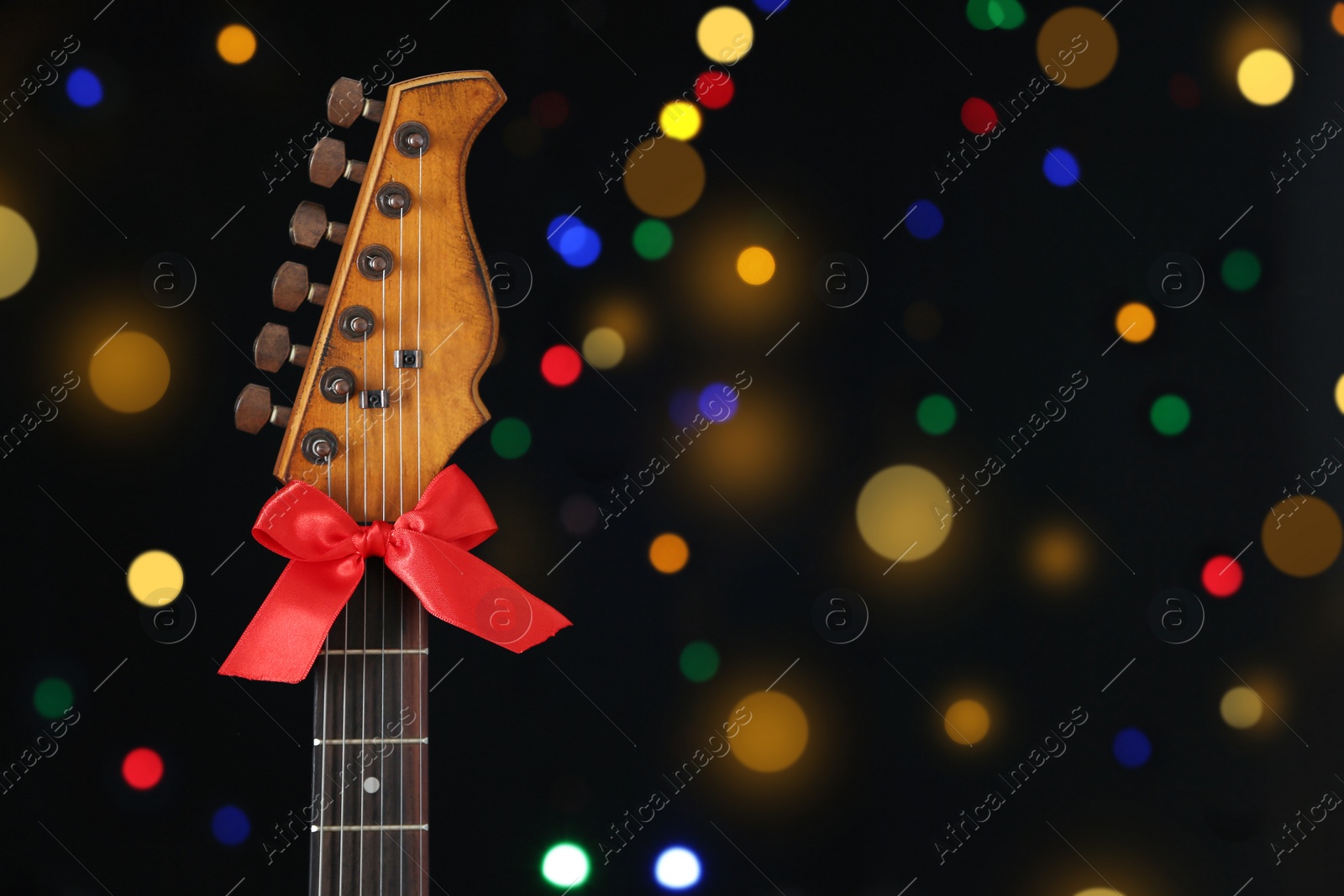 Photo of Guitar with bow against blurred lights, space for text. Christmas music