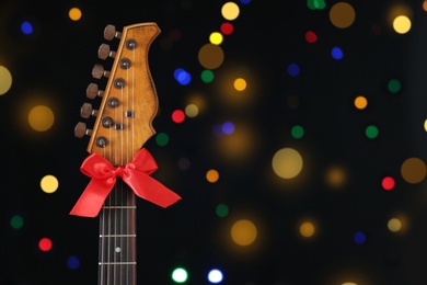 Photo of Guitar with bow against blurred lights, space for text. Christmas music