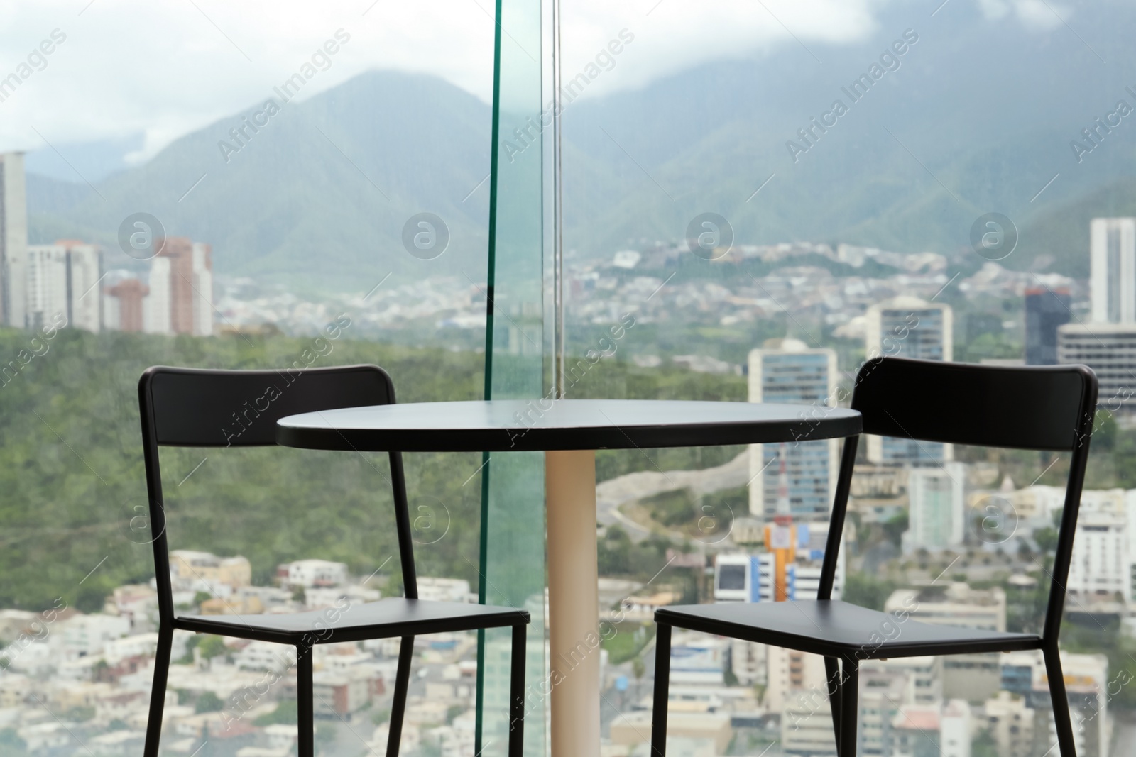 Photo of Coffee table and chairs against picturesque landscape of city in cafe