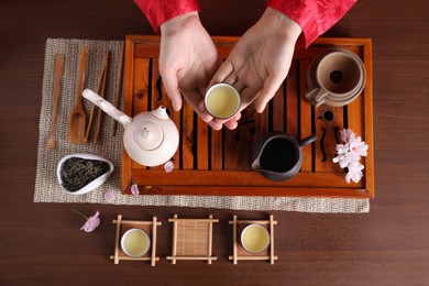Photo of Woman with cup of freshly brewed tea during traditional ceremony at wooden table, top view