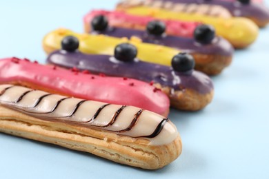 Photo of Delicious eclairs covered with glaze on light blue background, closeup