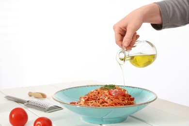 Photo of Food stylist pouring oil into spaghetti at white wooden table in photo studio, closeup