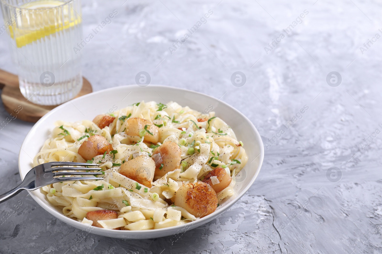 Photo of Delicious scallop pasta with spices served on gray textured table, closeup. Space for text