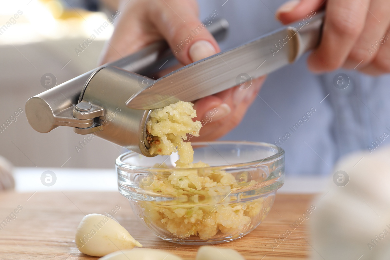 Photo of Woman squeezing garlic with press at wooden table indoors, closeup