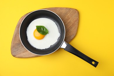 Photo of Pan with tasty fried egg on yellow background, top view