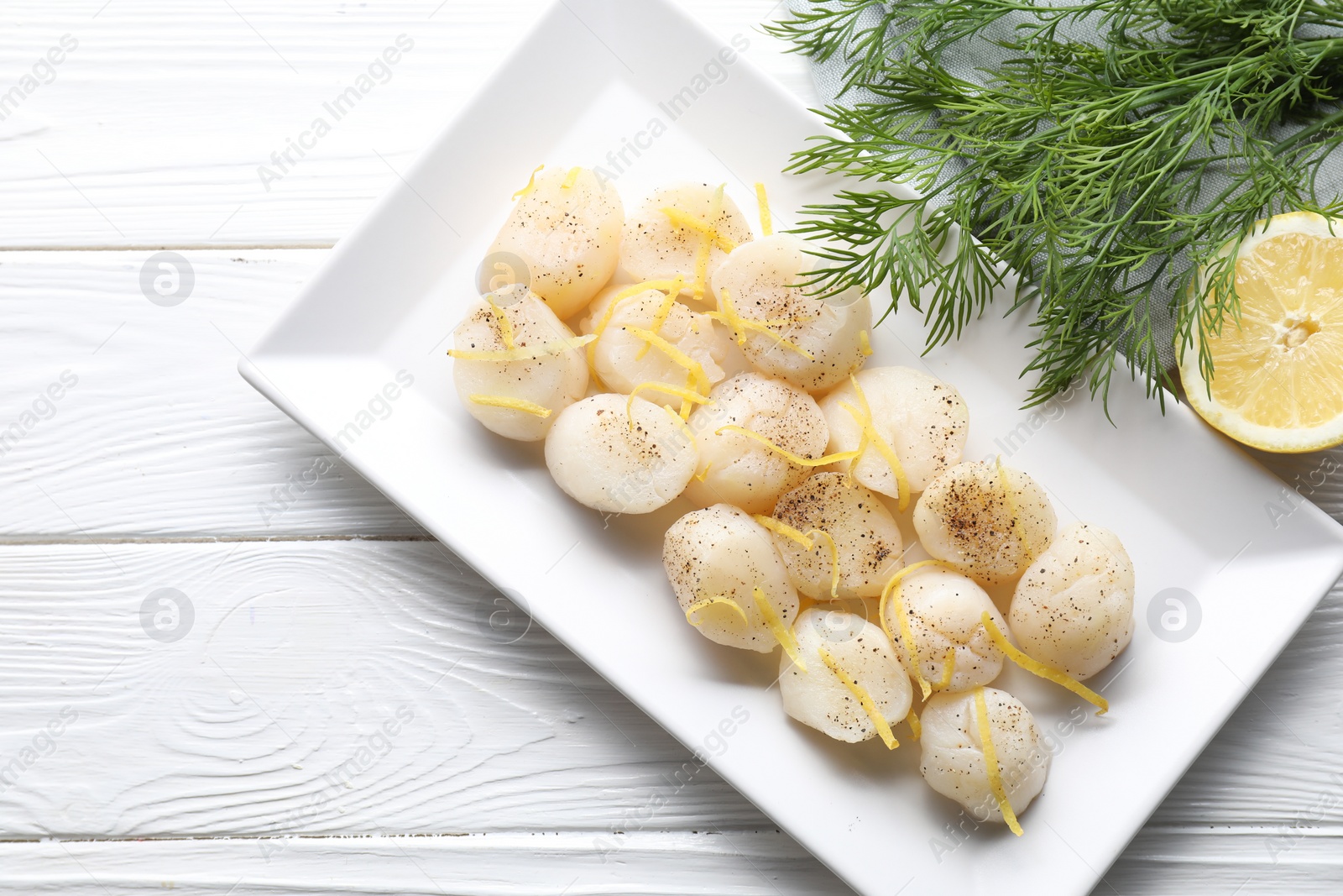 Photo of Raw scallops with milled pepper, lemon zest and dill on white wooden table, flat lay