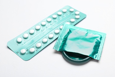 Photo of Condom and birth control pills on white background, closeup. Safe sex concept