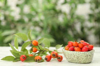 Ripe rose hip berries with green leaves on white wooden table outdoors