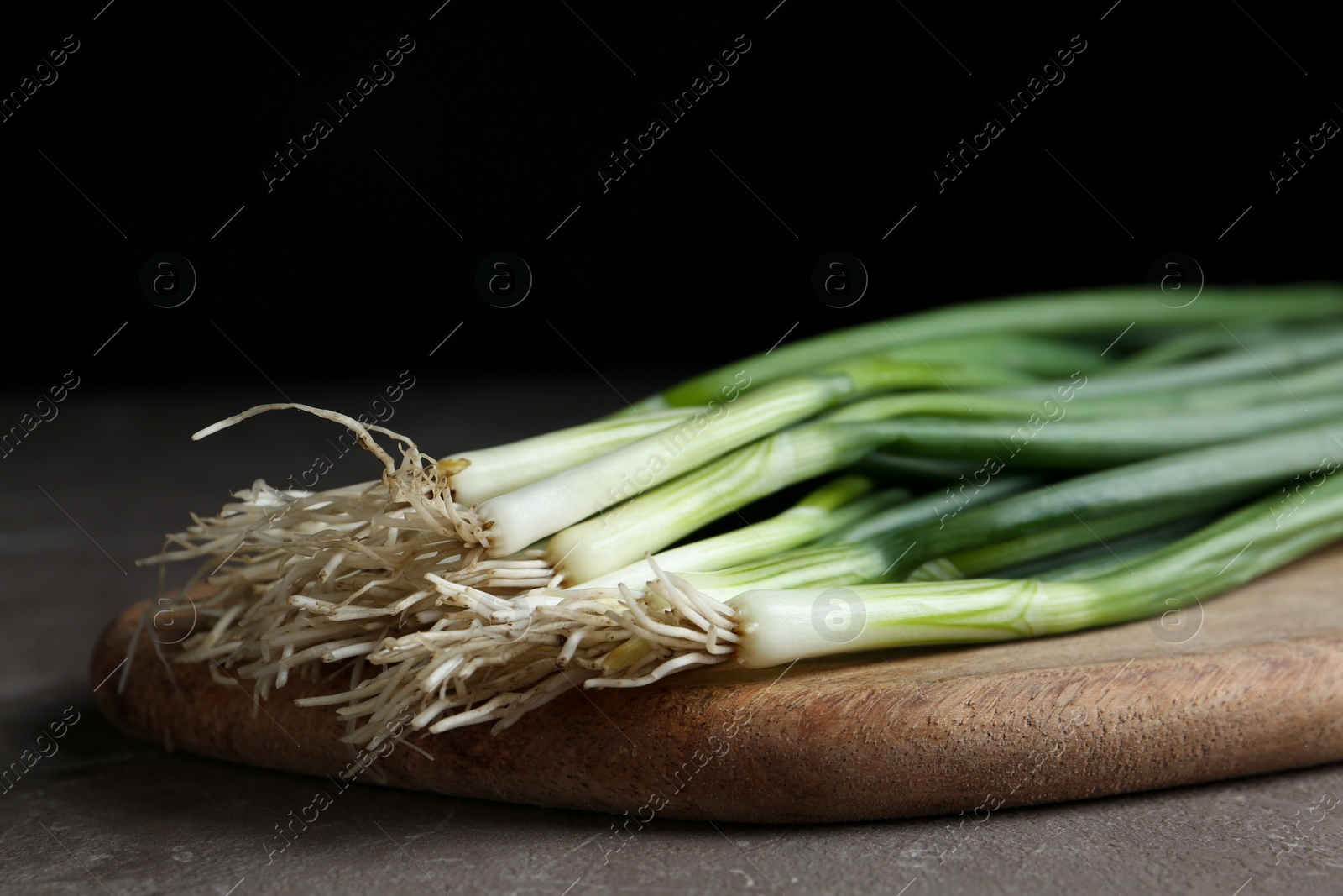 Photo of Fresh green spring onions on wooden board, closeup