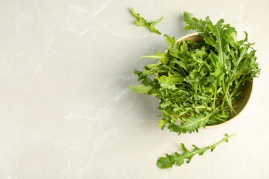 Fresh arugula in bowl on light grey marble table, flat lay. Space for text