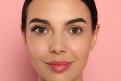 Photo of Beautiful young woman showing extended and ordinary eyelashes on pink background, closeup