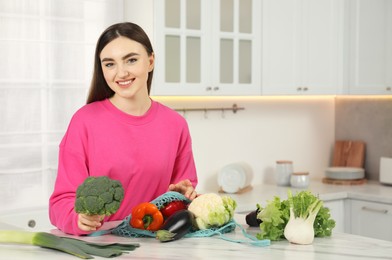 Photo of Woman with broccoli and string bag of fresh vegetables at light marble table in kitchen