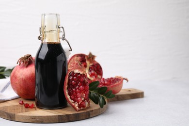 Photo of Tasty pomegranate sauce in bottle, branches and fruits on light table, closeup. Space for text