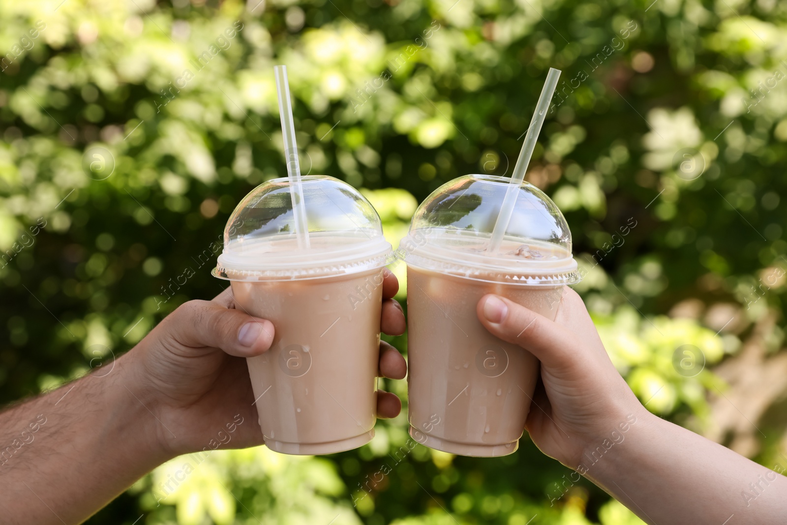 Photo of Man and woman toasting with plastic takeaway cups of delicious iced coffee outdoors, closeup