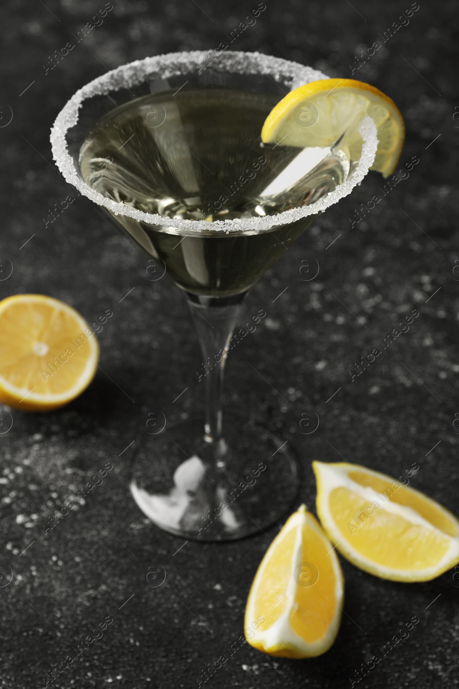 Photo of Martini glass of refreshing cocktail decorated with lemon slice and sugar on black textured table