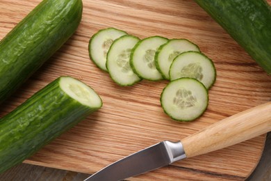 Photo of Cut cucumber and knife on wooden board, top view