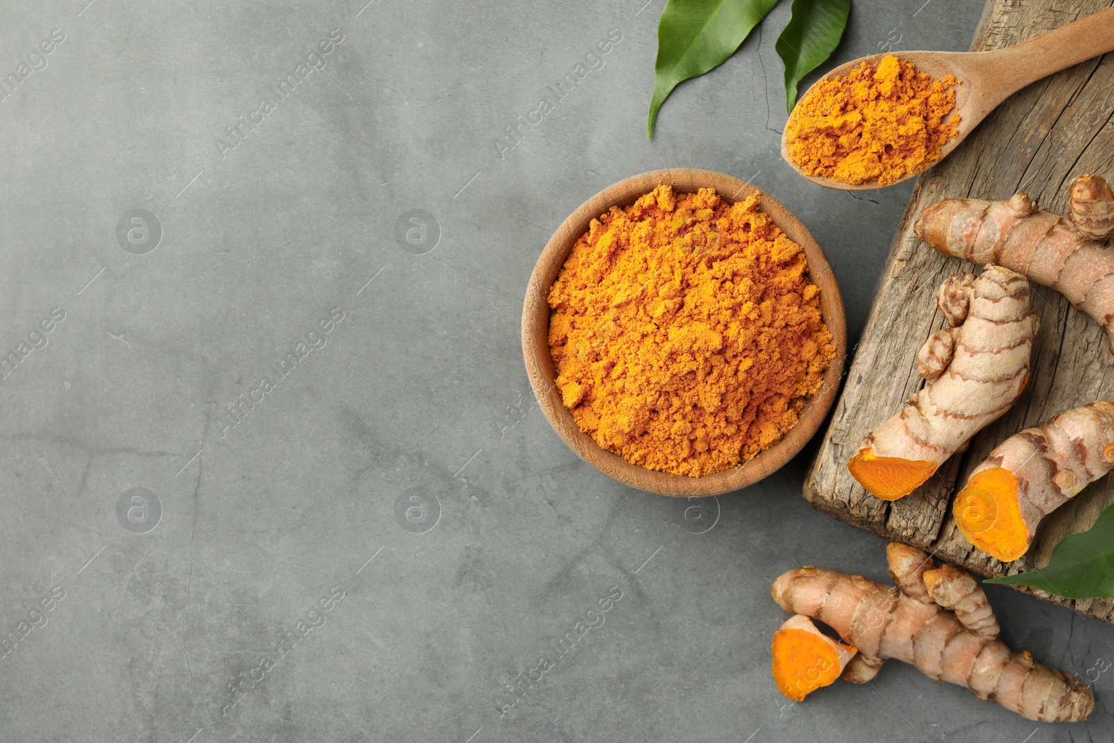 Photo of Aromatic turmeric powder and raw roots on grey table, flat lay. Space for text