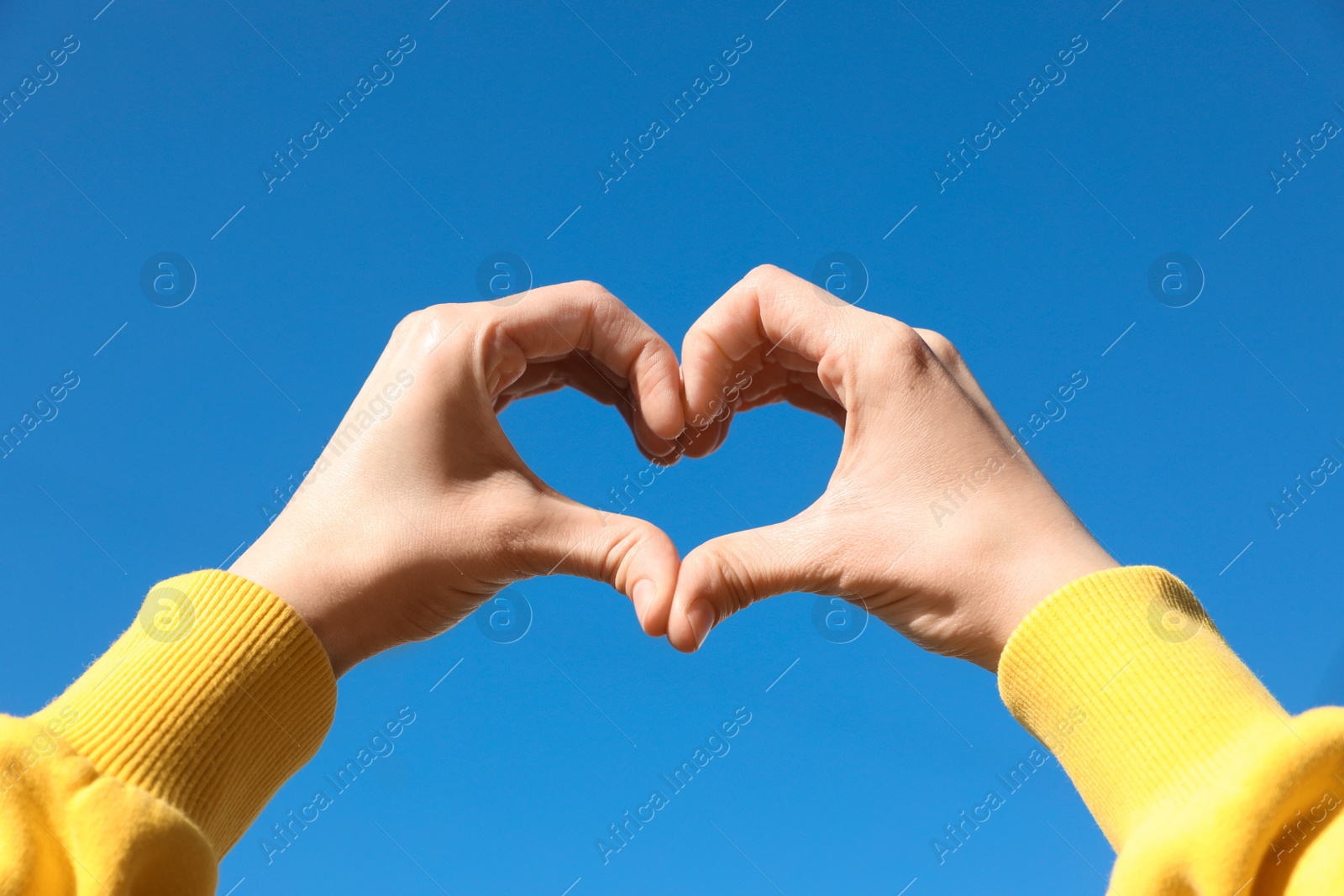 Photo of Woman showing heart against blue sky outdoors on sunny day, closeup of hands