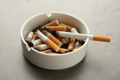 Photo of Ceramic ashtray full of cigarette stubs on grey table