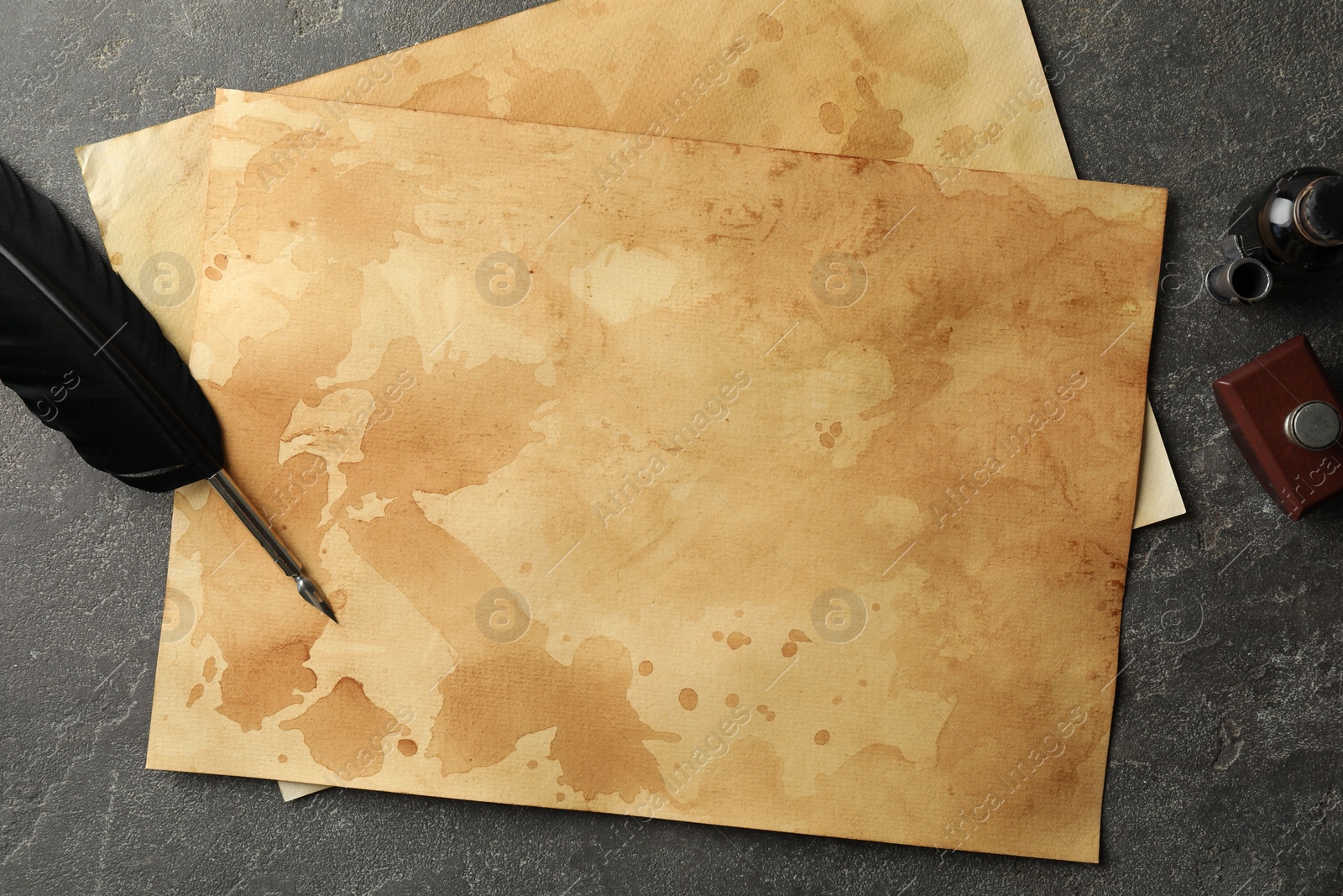 Photo of Black feather, inkwell and vintage parchment on grey table, flat lay