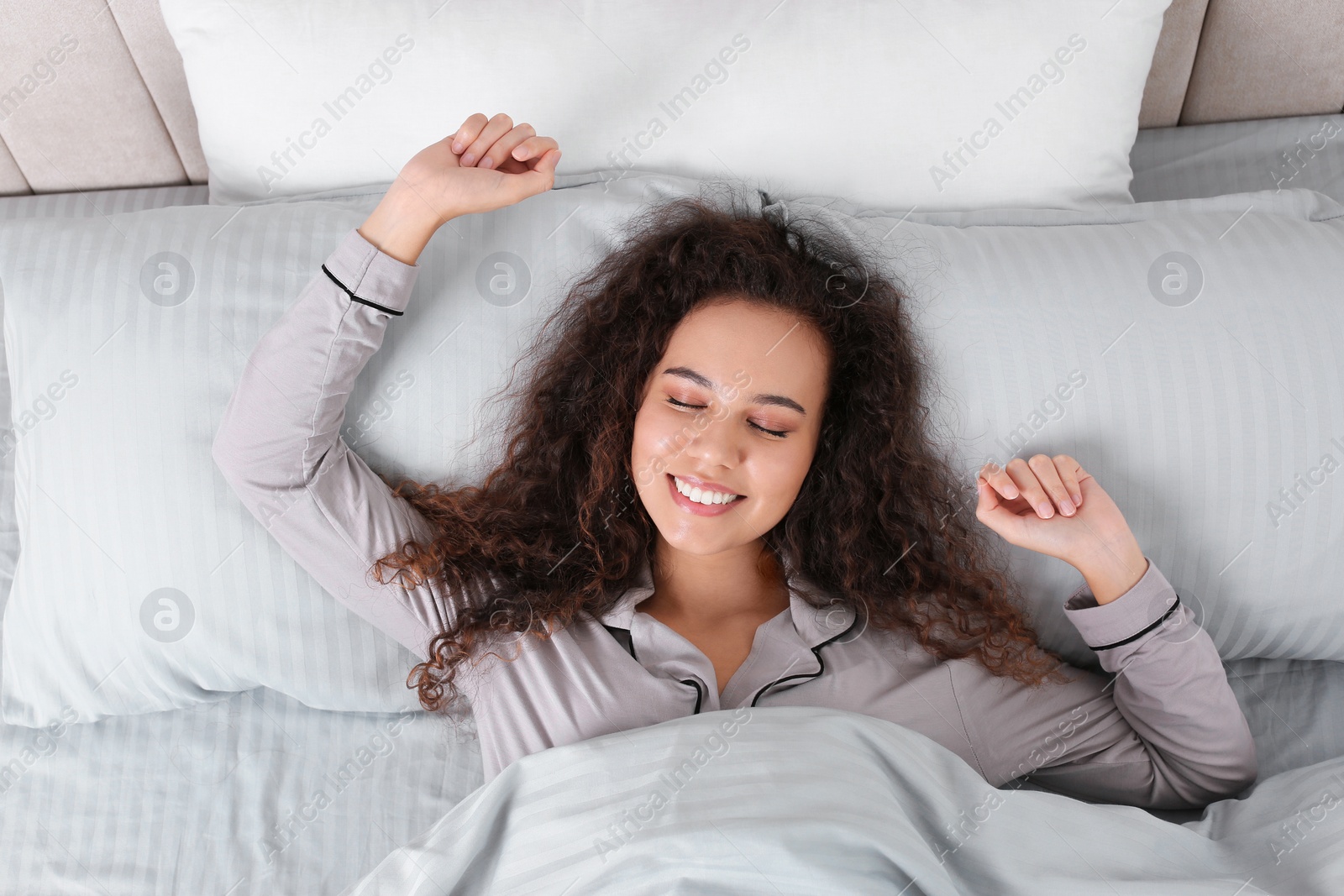 Photo of Beautiful African American woman stretching in bed, top view