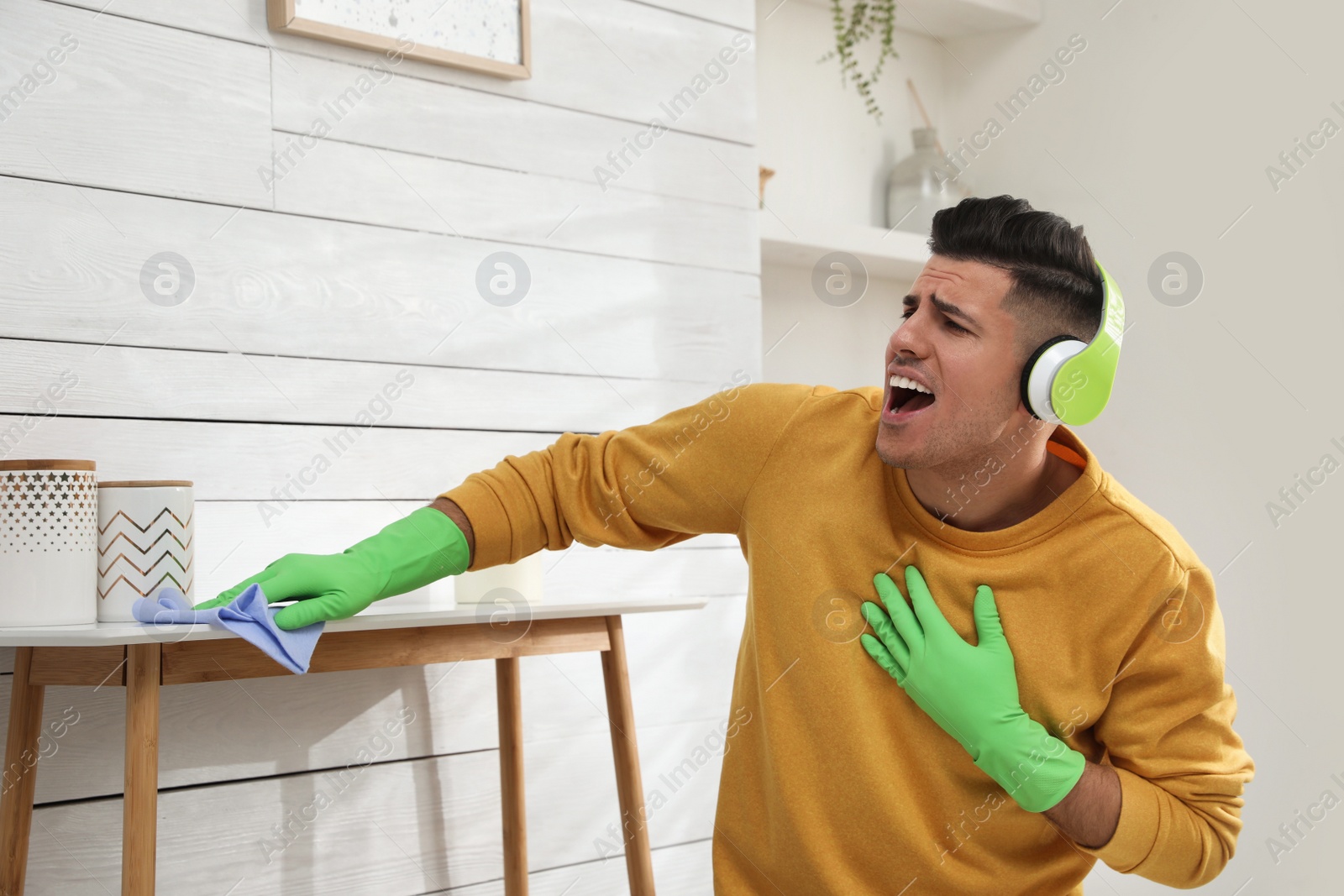 Photo of Man in headphones with rag singing while cleaning at home