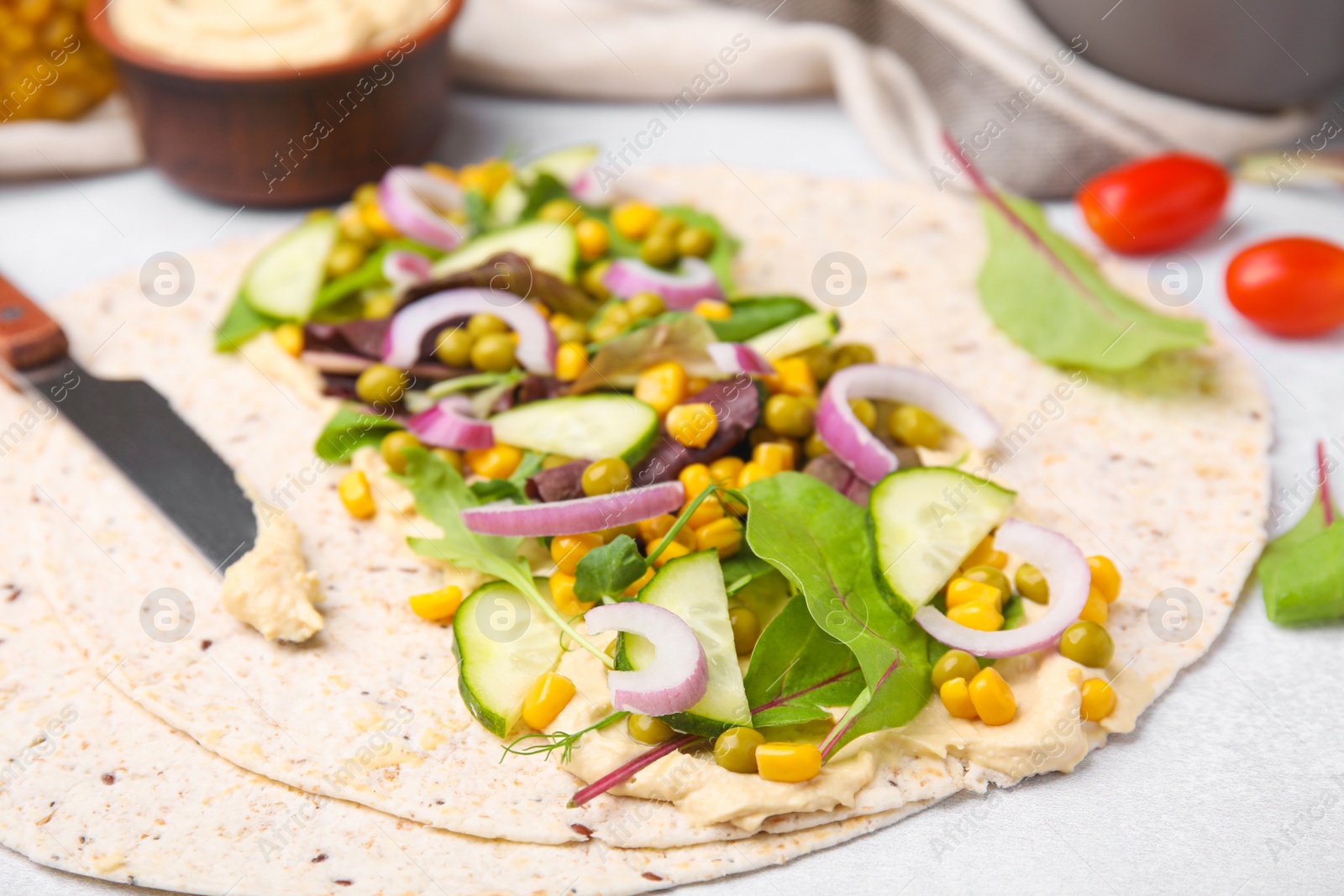 Photo of Tortilla with hummus and vegetables on table, closeup