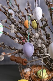 Photo of Beautiful willow branches with painted eggs on light grey background, closeup. Easter decor