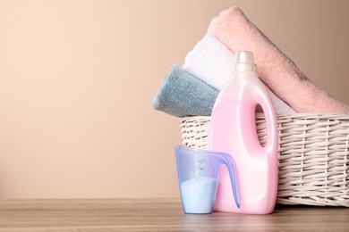 Photo of Detergents and basket with clean towels on table against color background, space for text. Laundry day