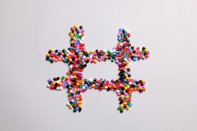 Photo of Hashtag symbol of colorful melty beads on light background, top view