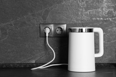 Photo of Electric kettle plugged into power socket on dark grey wall indoors