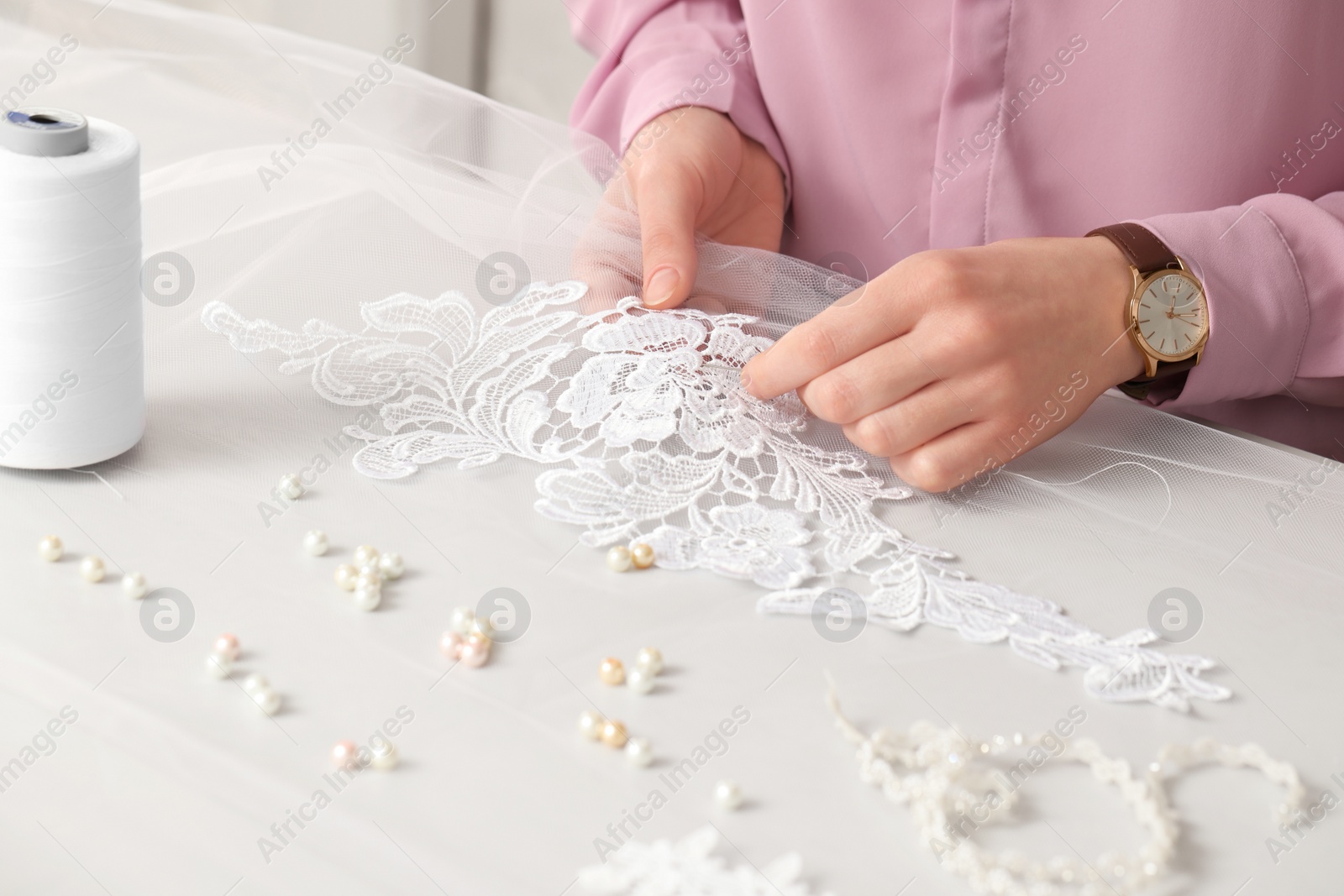 Photo of Dressmaker working with beautiful white lace at table in atelier, closeup