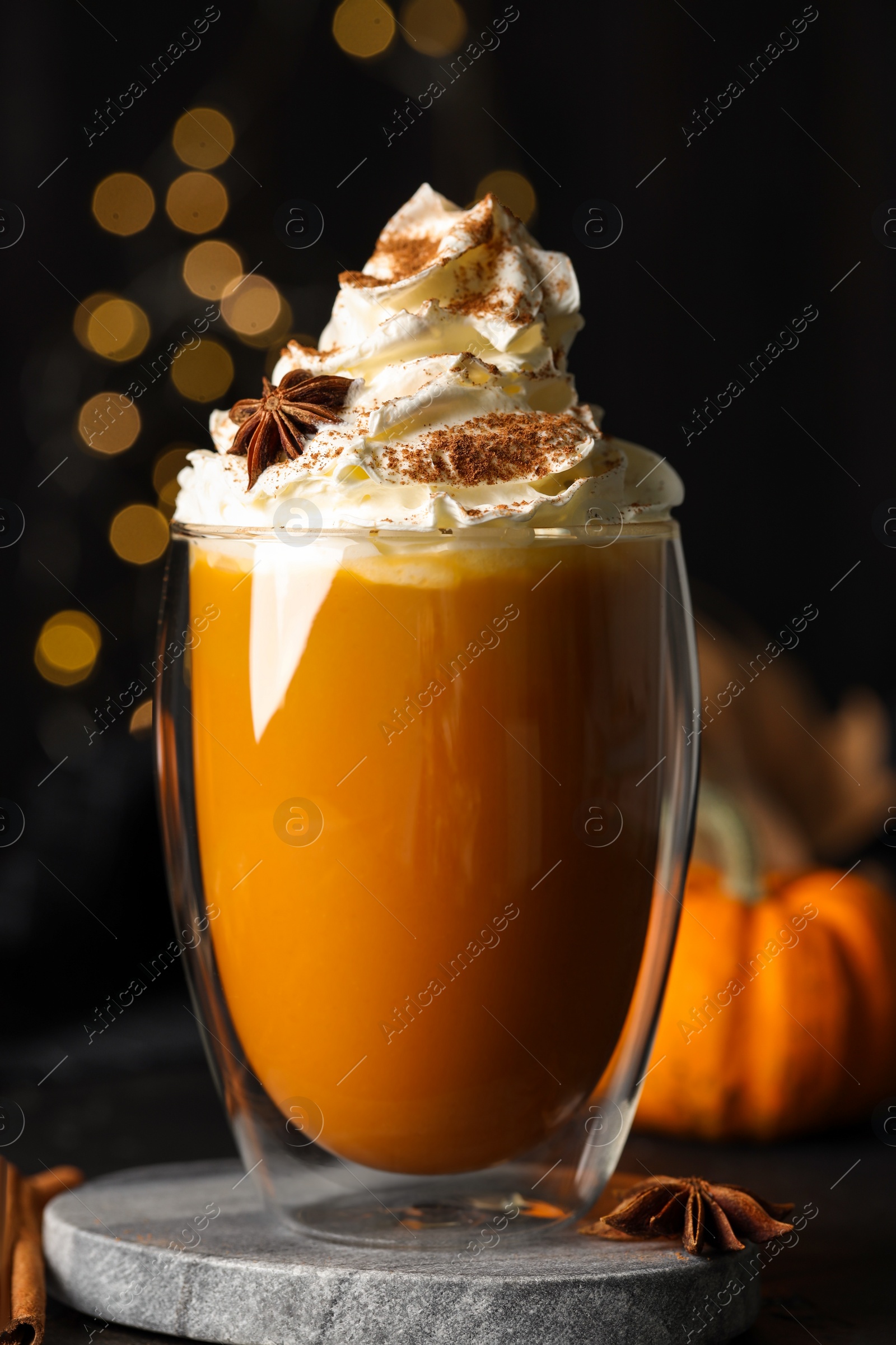 Photo of Glass of pumpkin spice latte with whipped cream and ingredients on black table, closeup