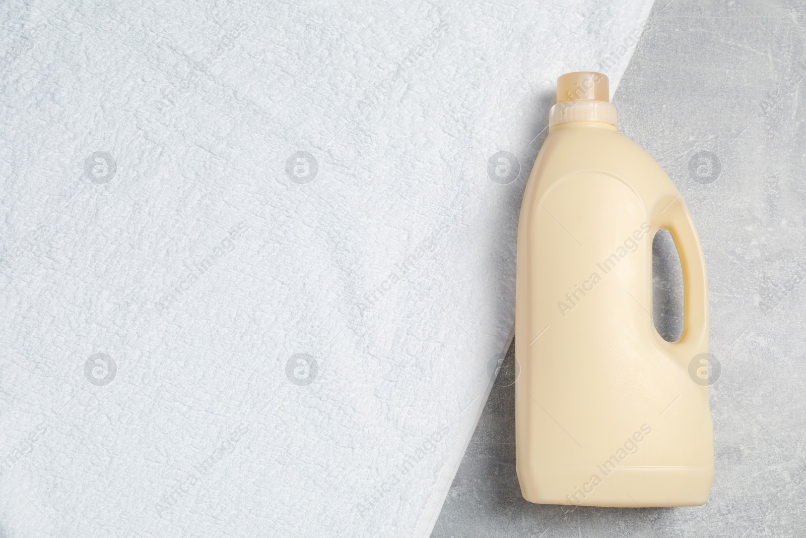 Photo of Bottle of laundry detergent and clean towel on light grey table, top view. Space for text