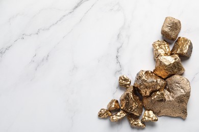 Pile of shiny gold nuggets on white marble table, flat lay. Space for text