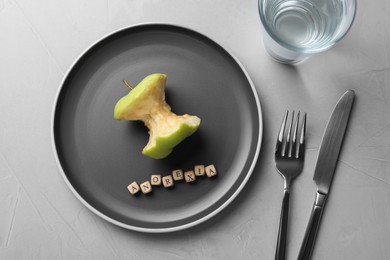 Photo of Cutlery, glass near plate with apple core and word Anorexia made of cubes on light table, flat lay