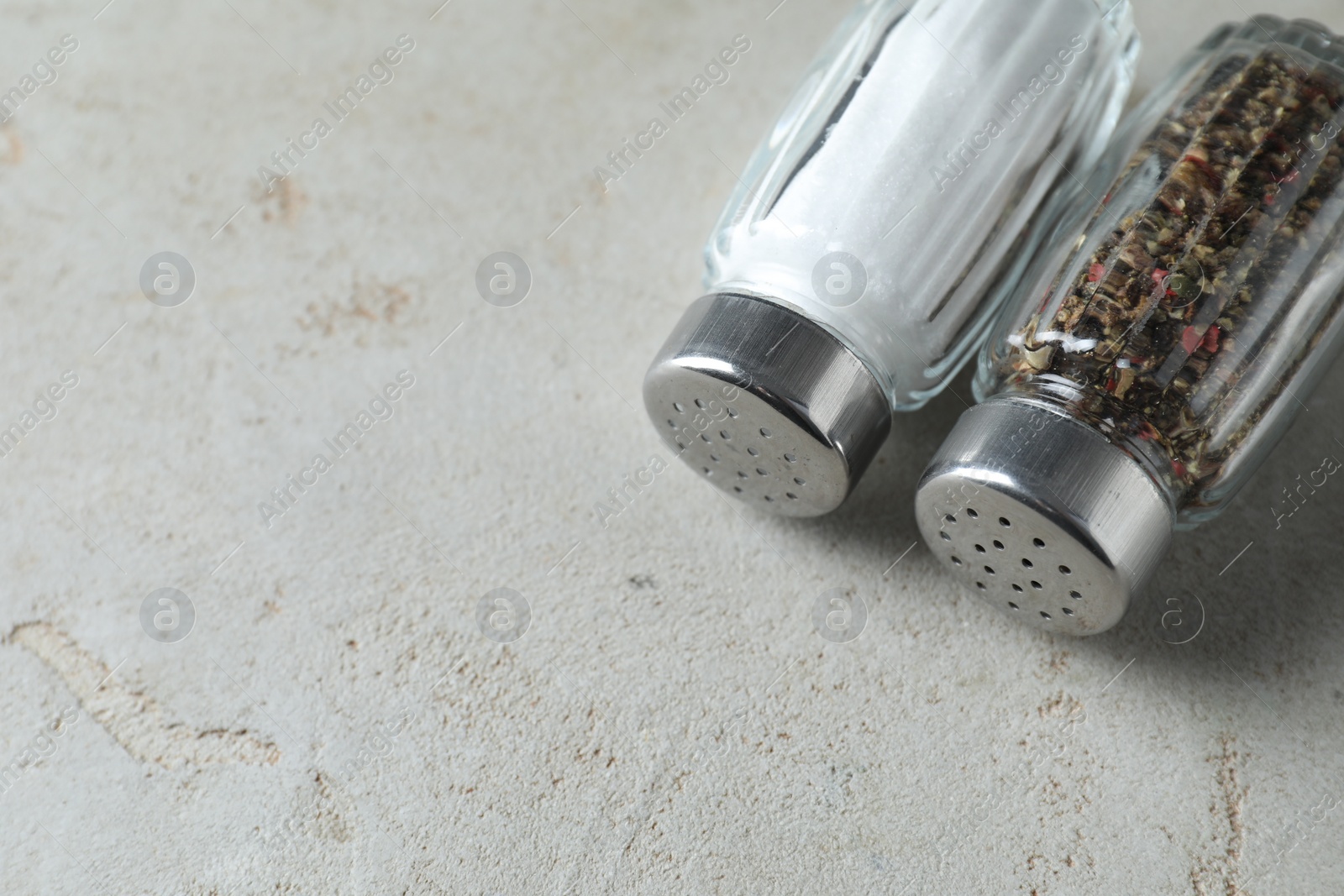 Photo of Salt and pepper shakers on light textured table. Space for text