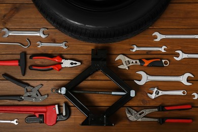 Car wheel, scissor jack and different tools on wooden surface, flat lay