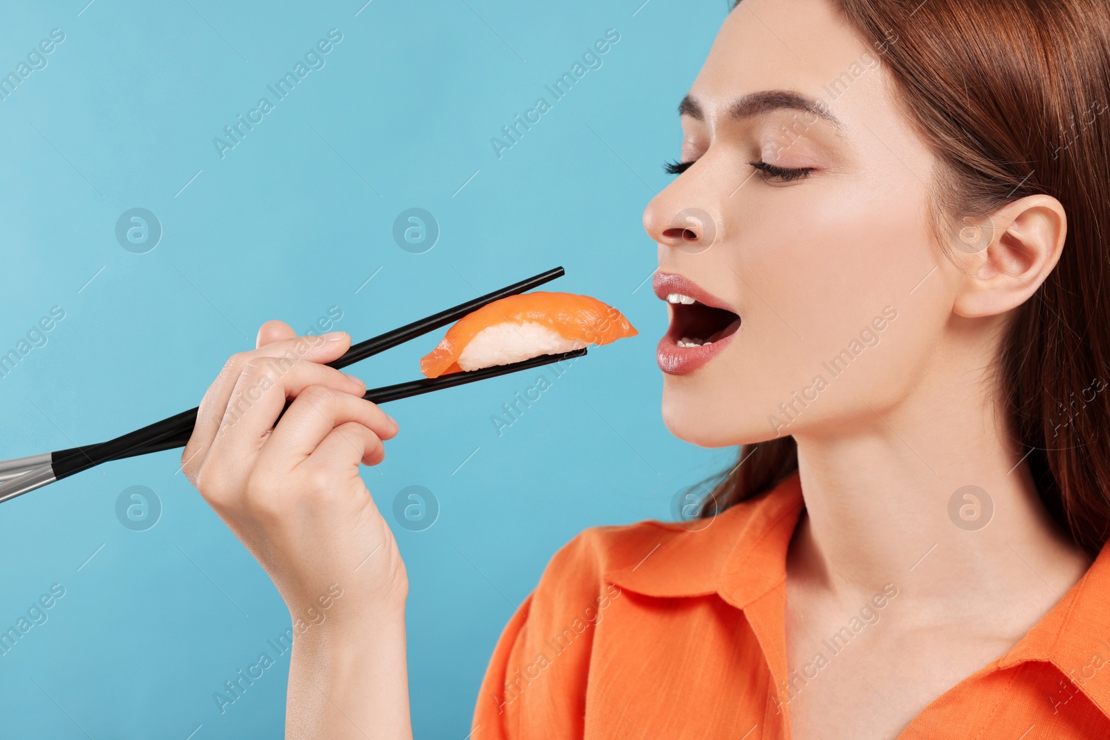 Photo of Beautiful young woman eating sushi with chopsticks on light blue background